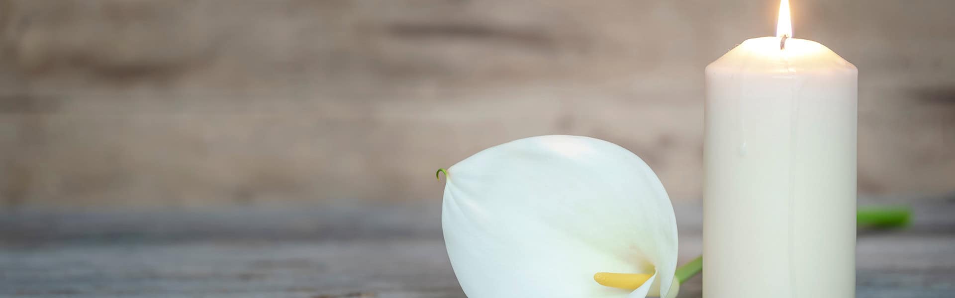 WHITE CALLA LILY FLOWER NEXT TO A LIGHTED CANDLE ON WOODEN BACKGROUND. / shutterstock.com